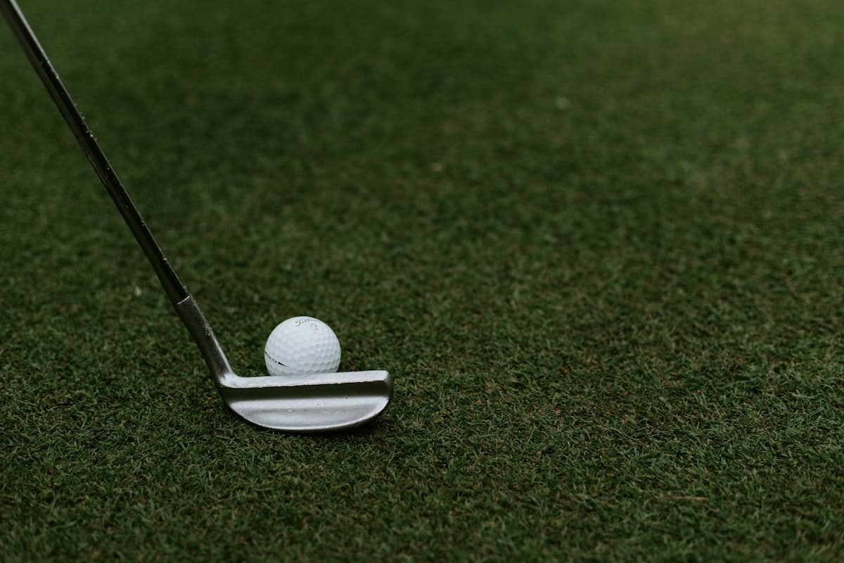Una bola de golf junto a un putter sobre el green, a pocos centímetros del hoyo
