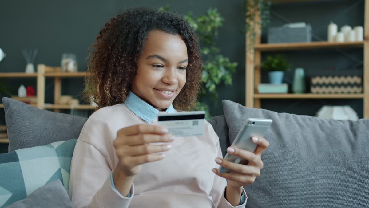 Persona sosteniendo una tarjeta bancaria mientras utiliza su teléfono móvil